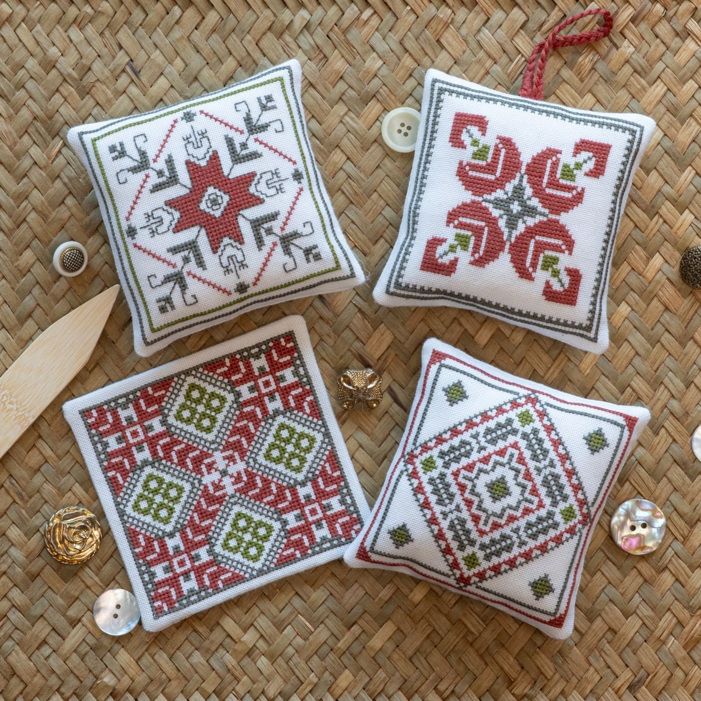 Four cross stitch folk embroidery square ornaments with geometric patterns on a woven placemat