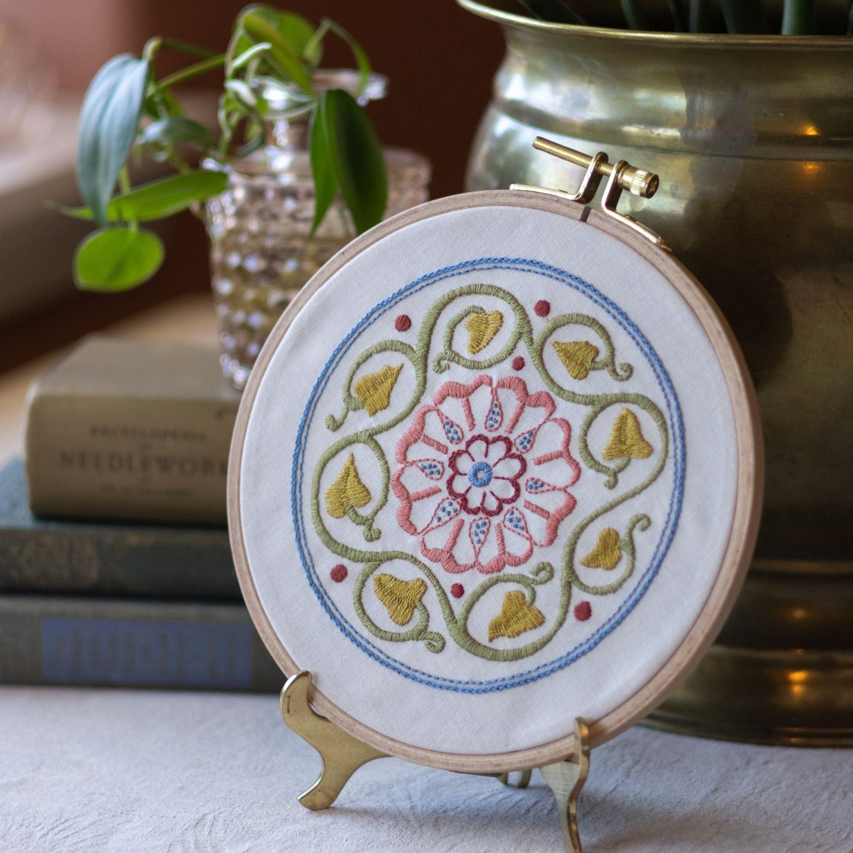 embroidery hoop with rose floral design on table with plants and books