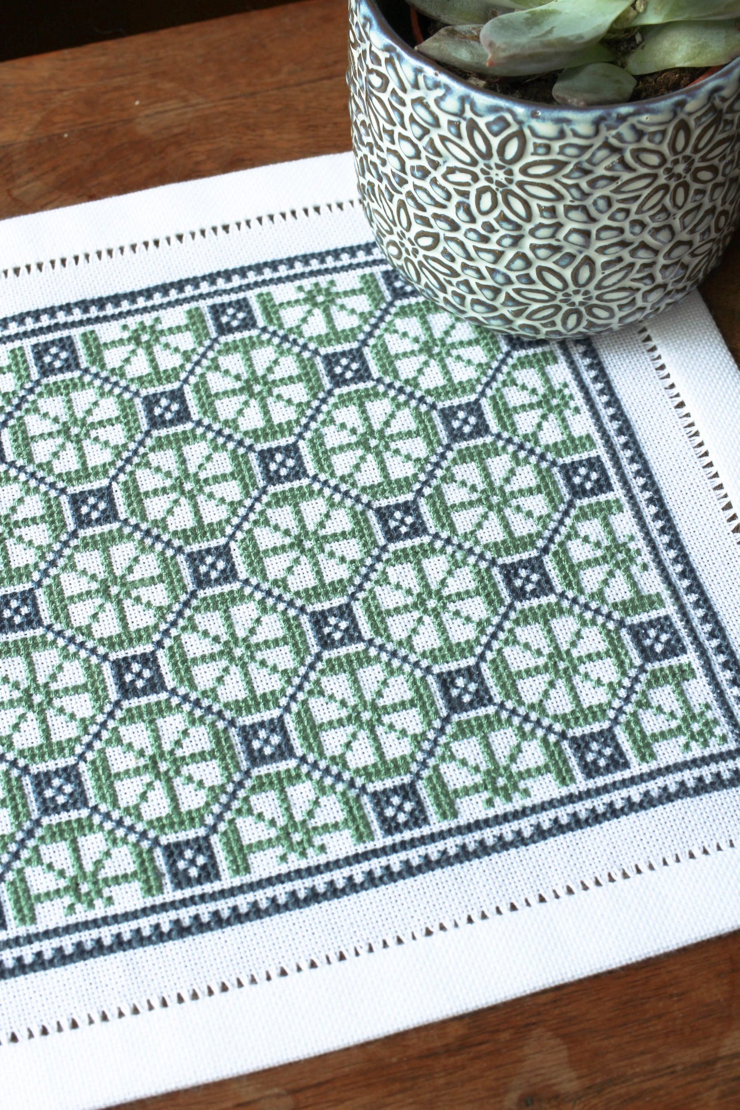 folk embroidery table mat with green and blue design and plant