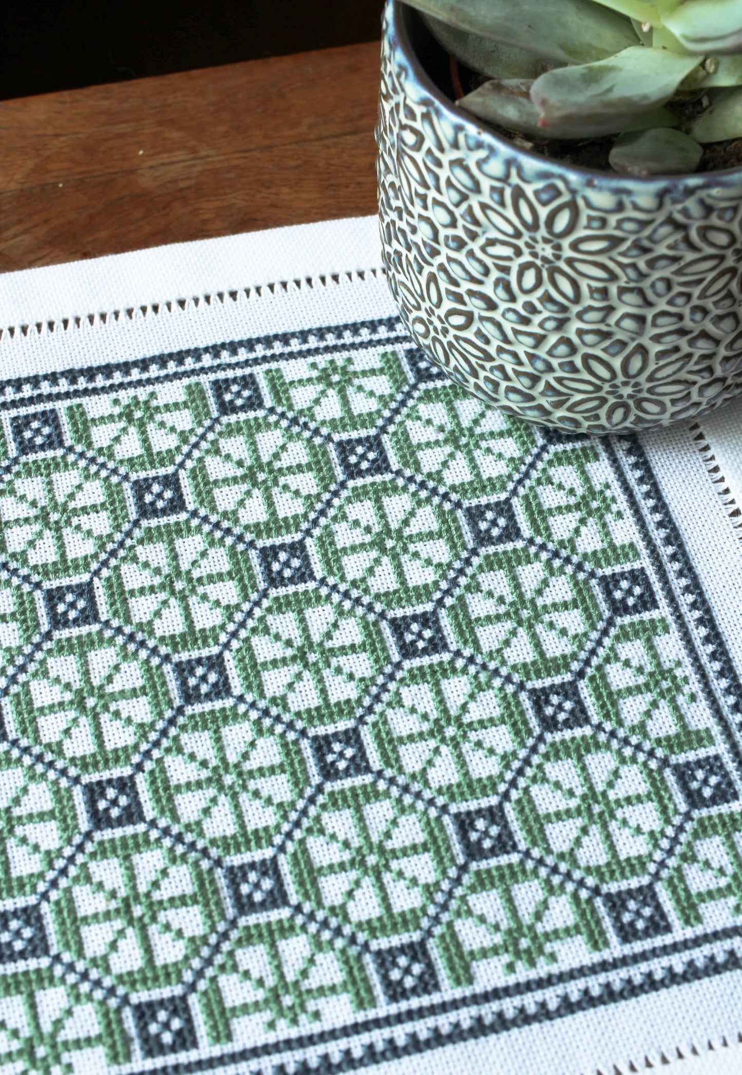folk embroidery table mat with green and blue design and plant