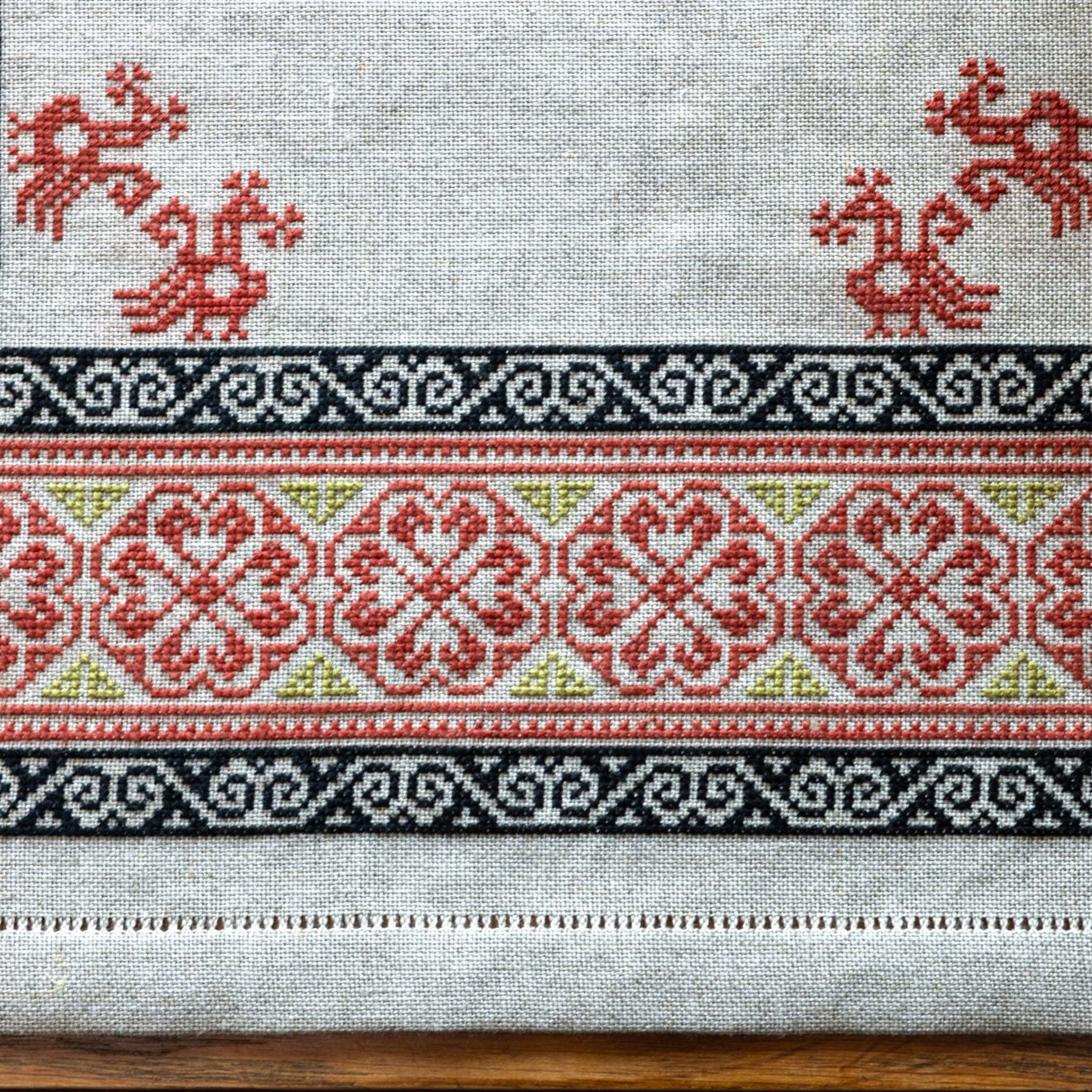 Close-up of a cross-stitched pattern with red and black designs on a white fabric background.