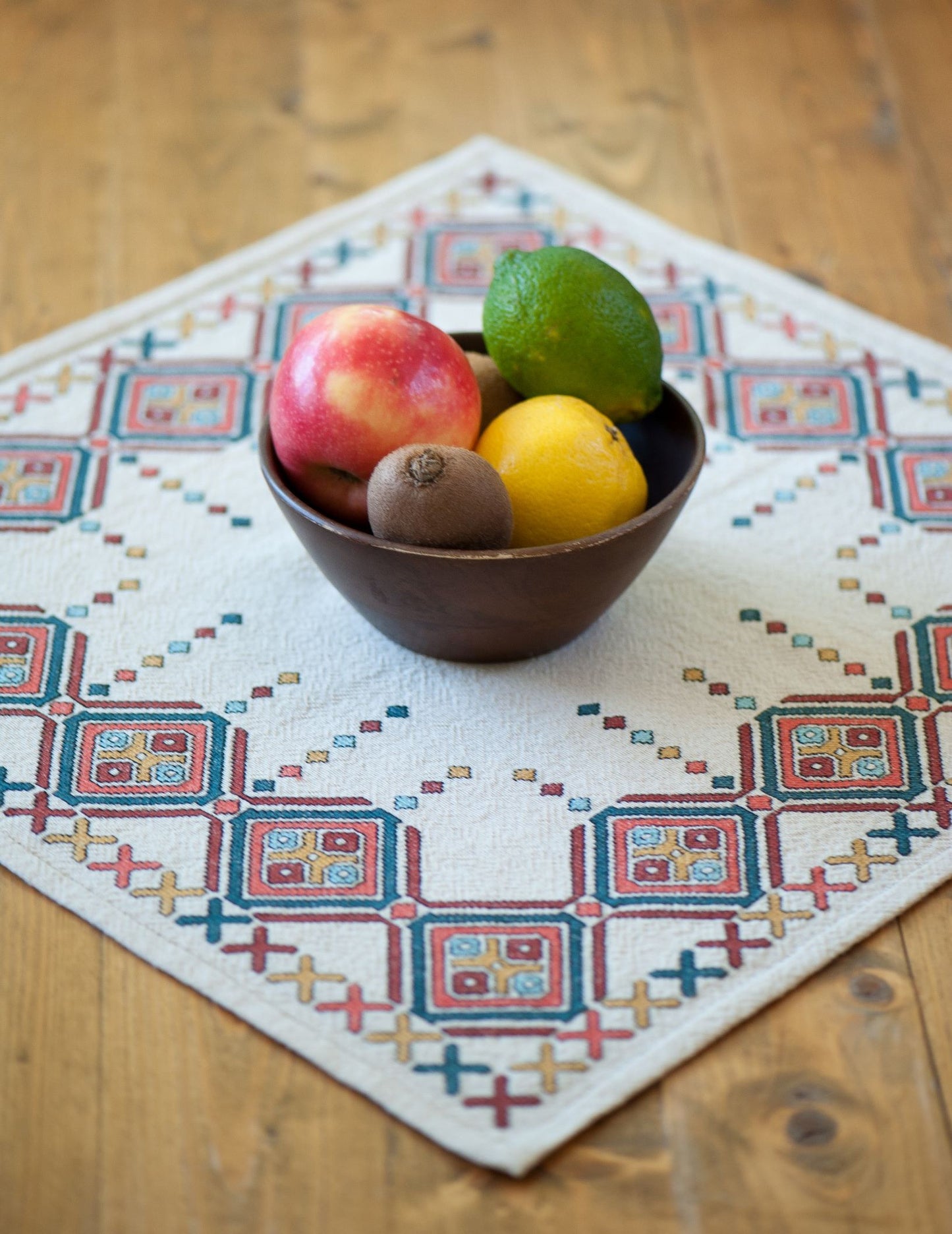 Bowl of fruit on a cross stitch table square with geometric pattern