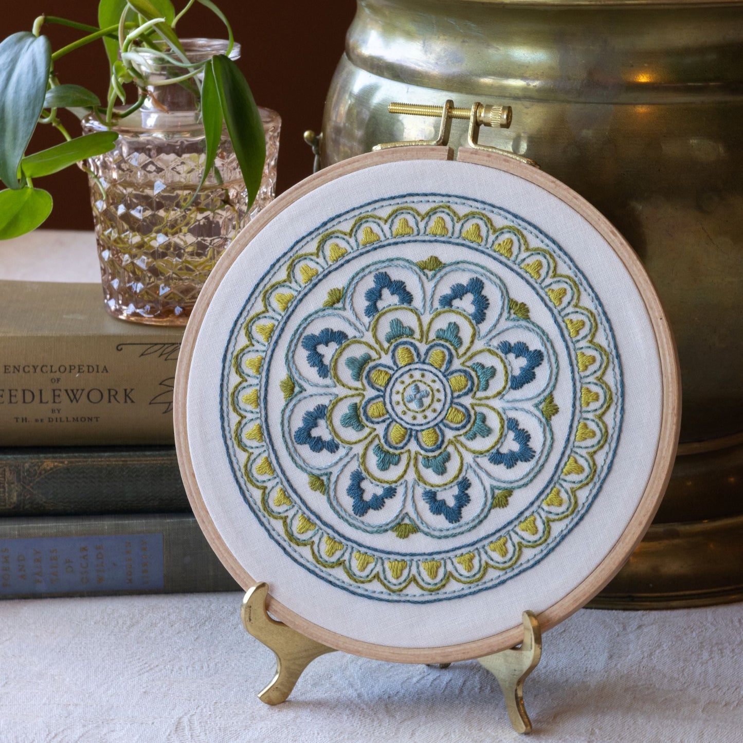 Decorative mandala embroidery, placed on a surface with books and plants in the background.