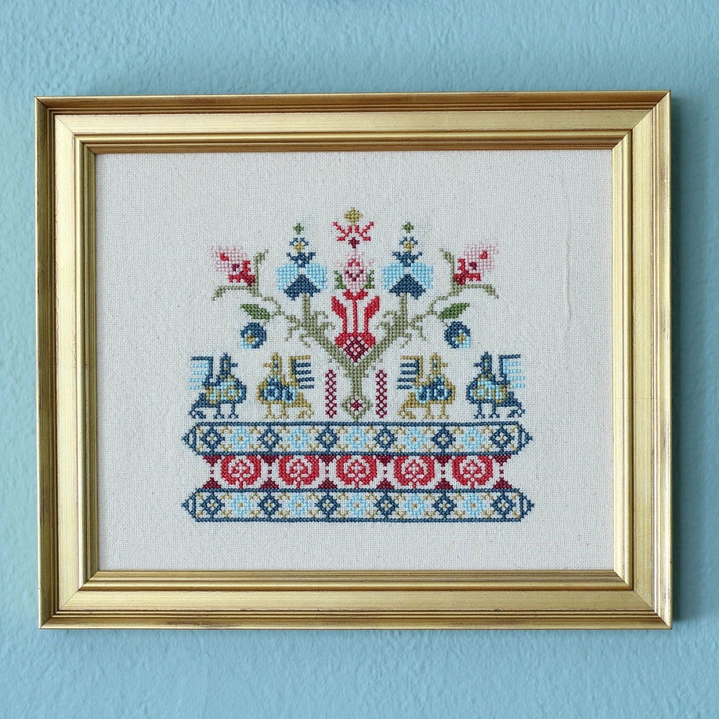 Framed cross-stitched artwork on a light blue wall