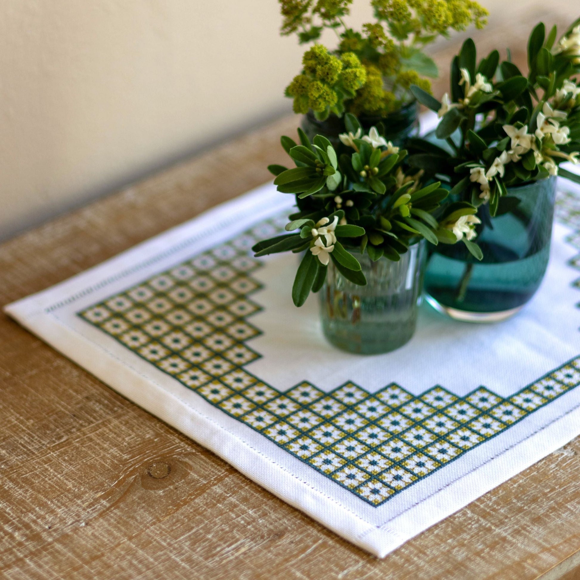 Decorative table mat with geometric pattern on a wooden surface with floral vases.