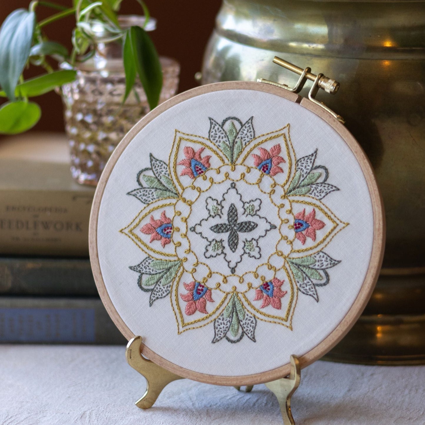 Embroidered mandala hoop art on a stand with books and plants in the background