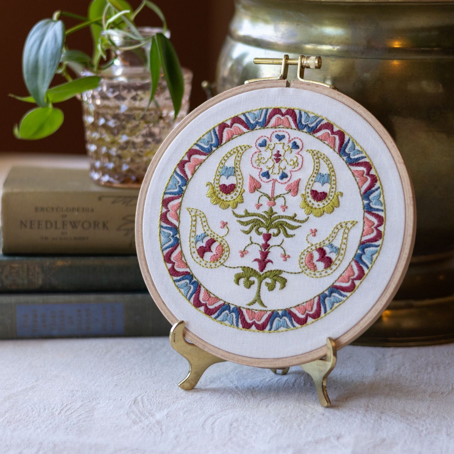 embroidery hoop with tree of life design on table next to books and plant