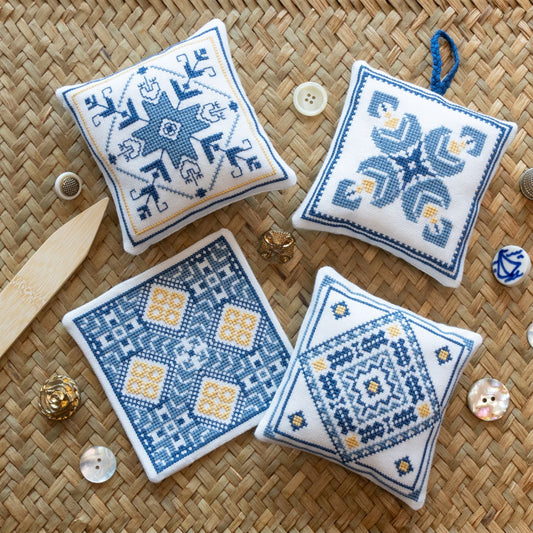 Four embroidered square cushions with blue and white patterns on a woven surface.