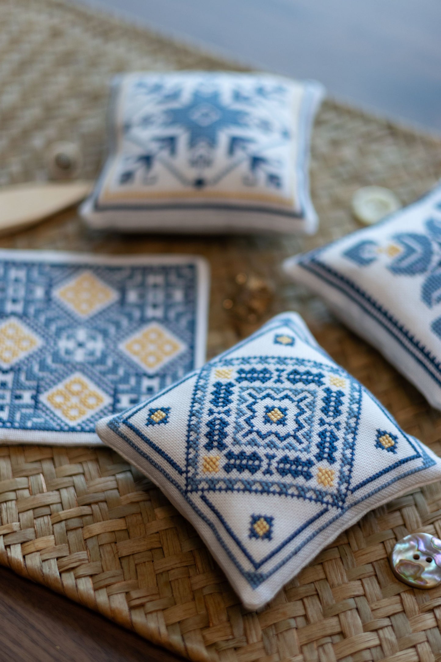 Decorative cross stitch ornaments with blue and white geometric patterns on a woven placemat