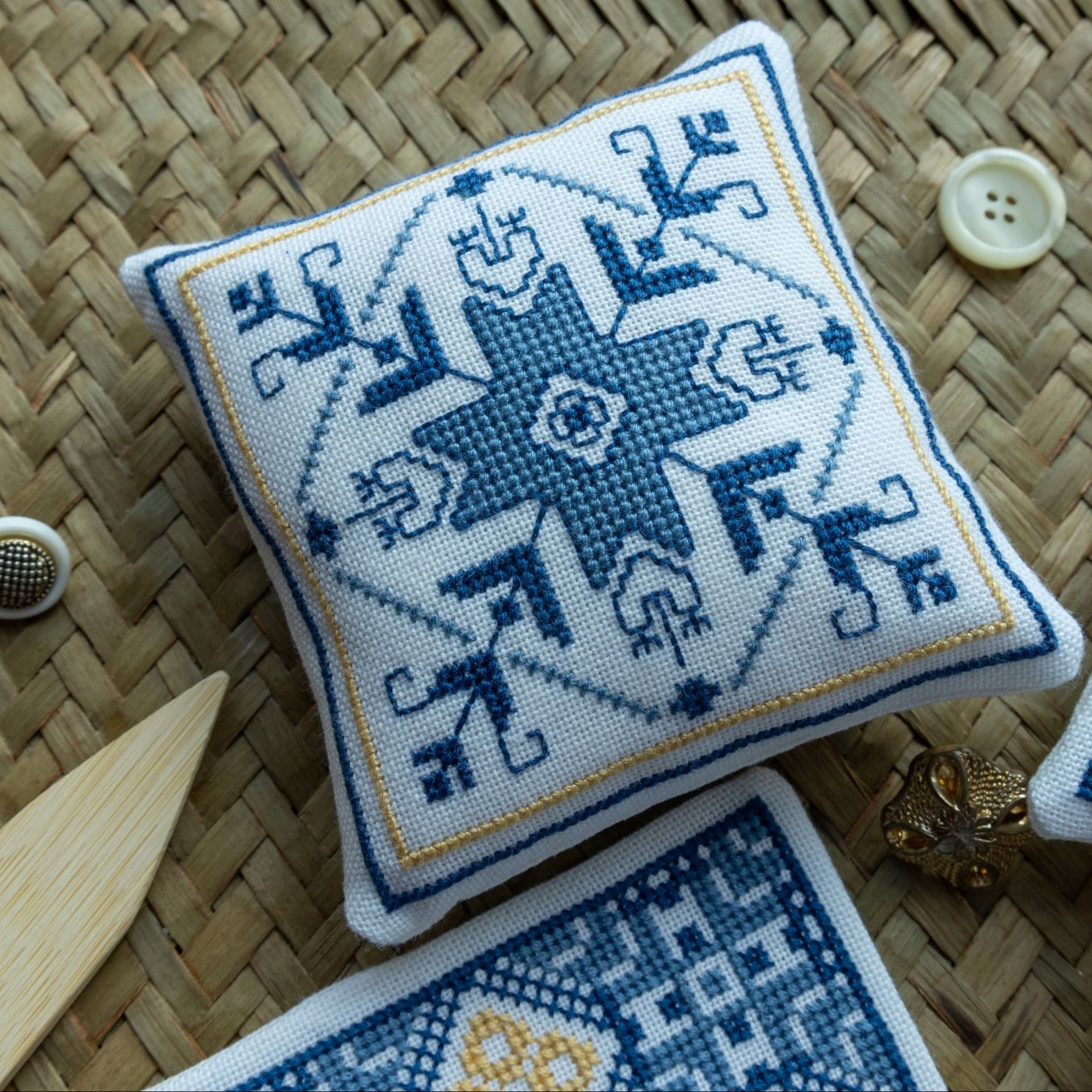 Cross-stitched pillow with blue and white pattern on a woven surface