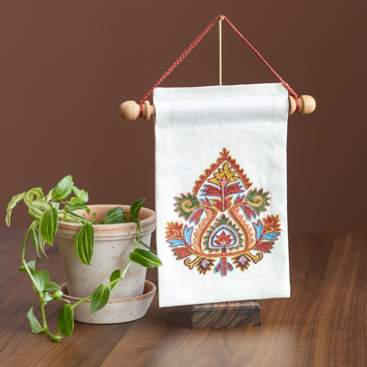 greek folk embroidery mini wall hanging with floral motif on a table with plant