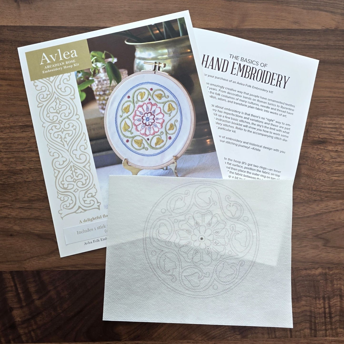 Embroidery kit with patterned fabric, instruction sheet on a wooden surface.