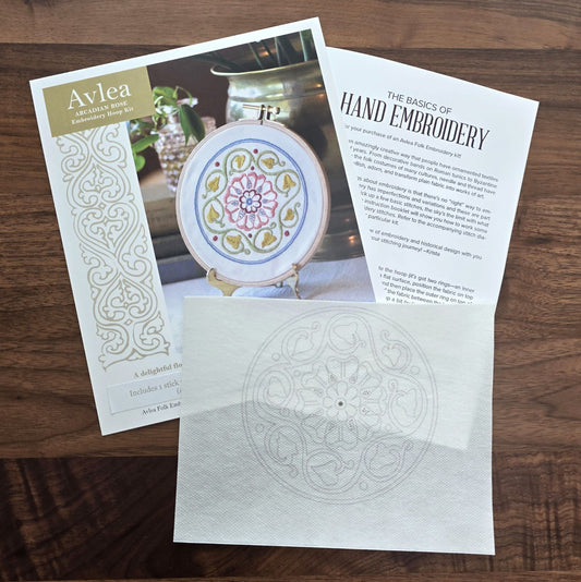 Embroidery kit with patterned fabric, instruction sheet on a wooden surface.