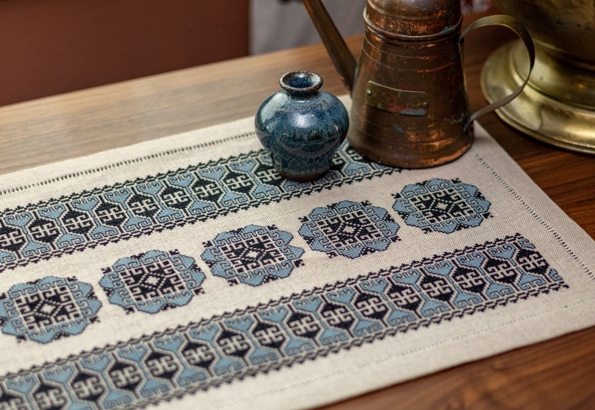 cross stitch folk embroidery with blue floral motif on flax linen with copper jug and vase