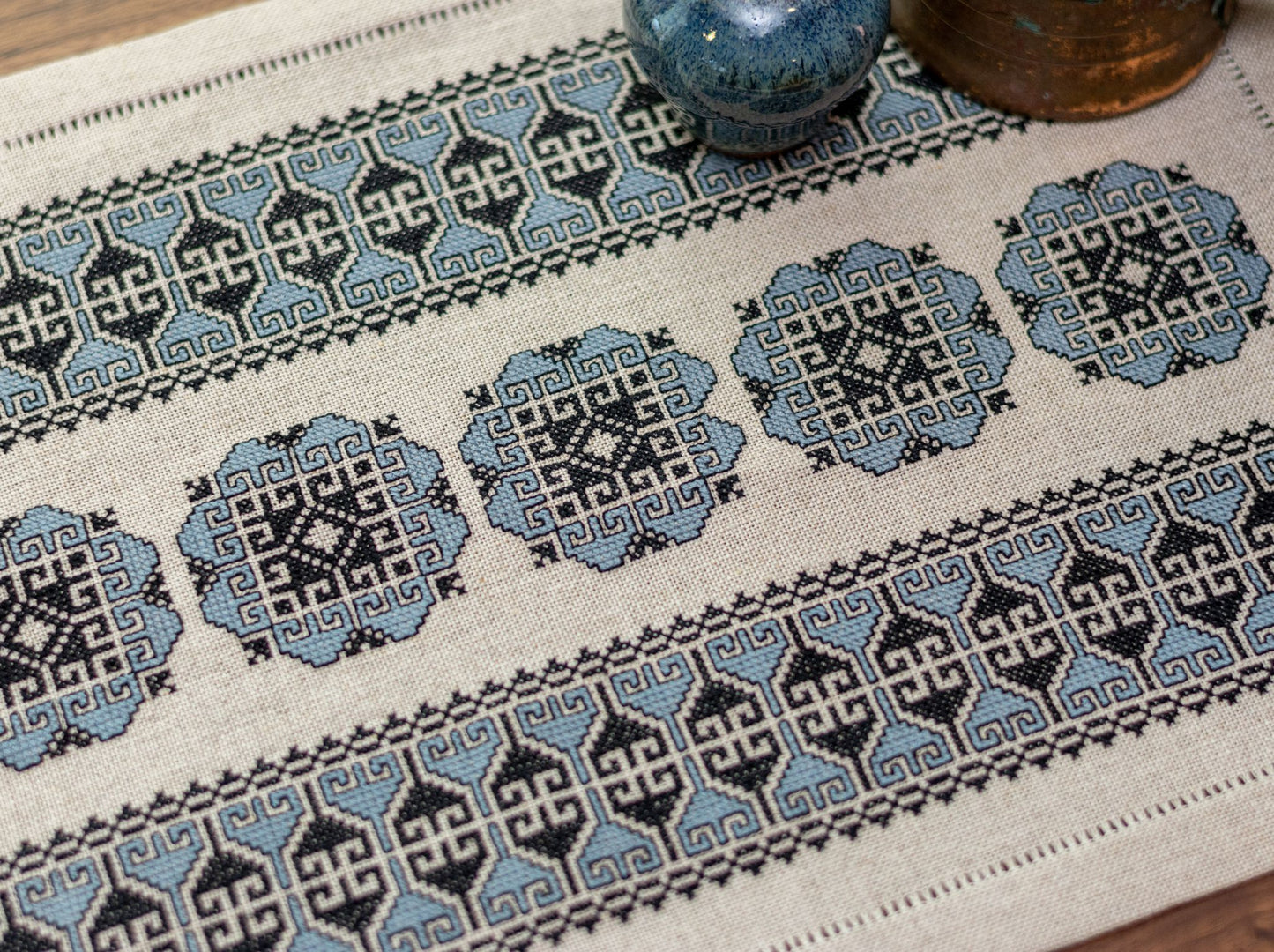 cross stitch folk embroidery with blue floral motif on flax linen with copper jug and vase