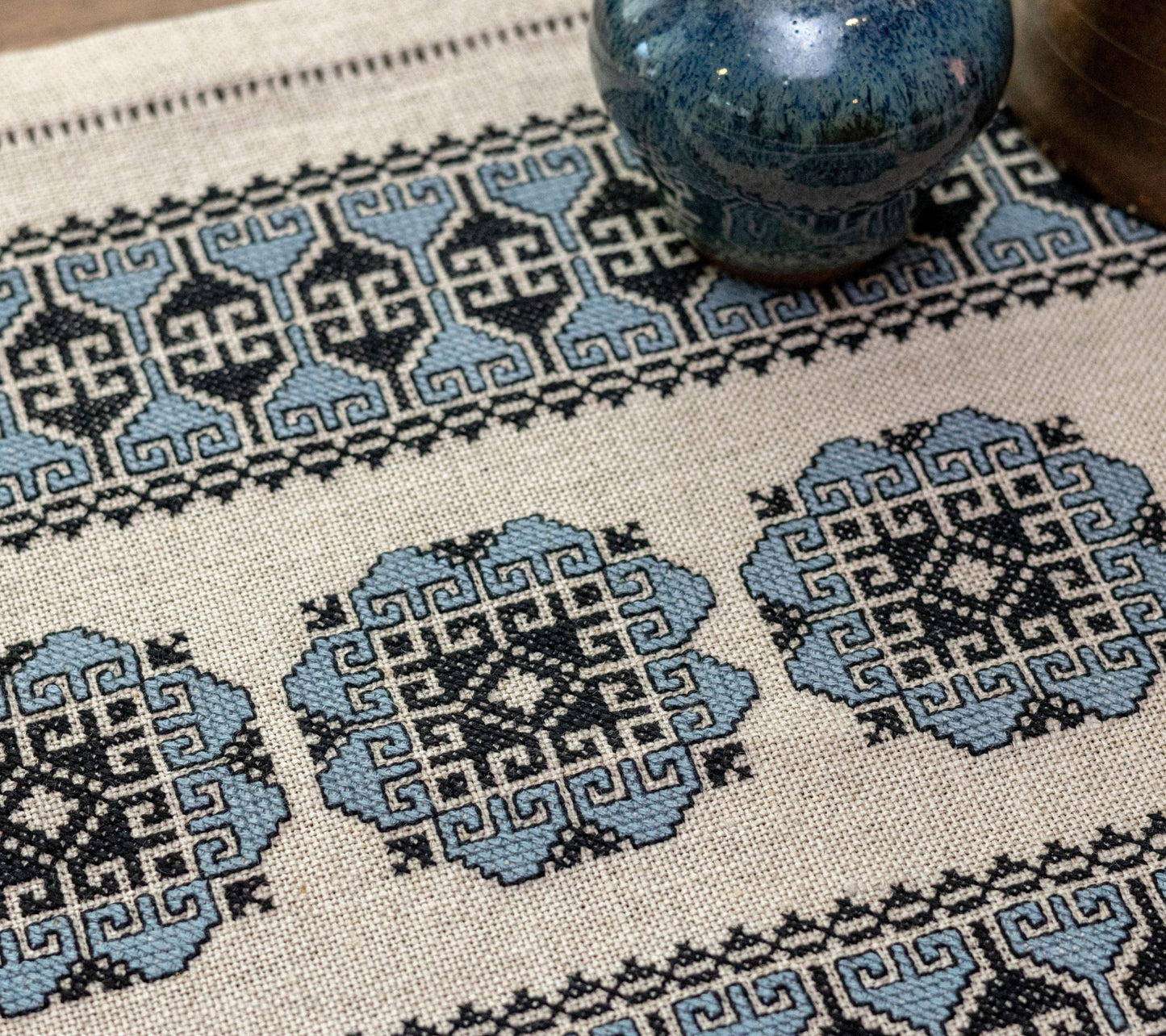 closeup of cross stitch folk embroidery with blue floral motif on flax linen with vase