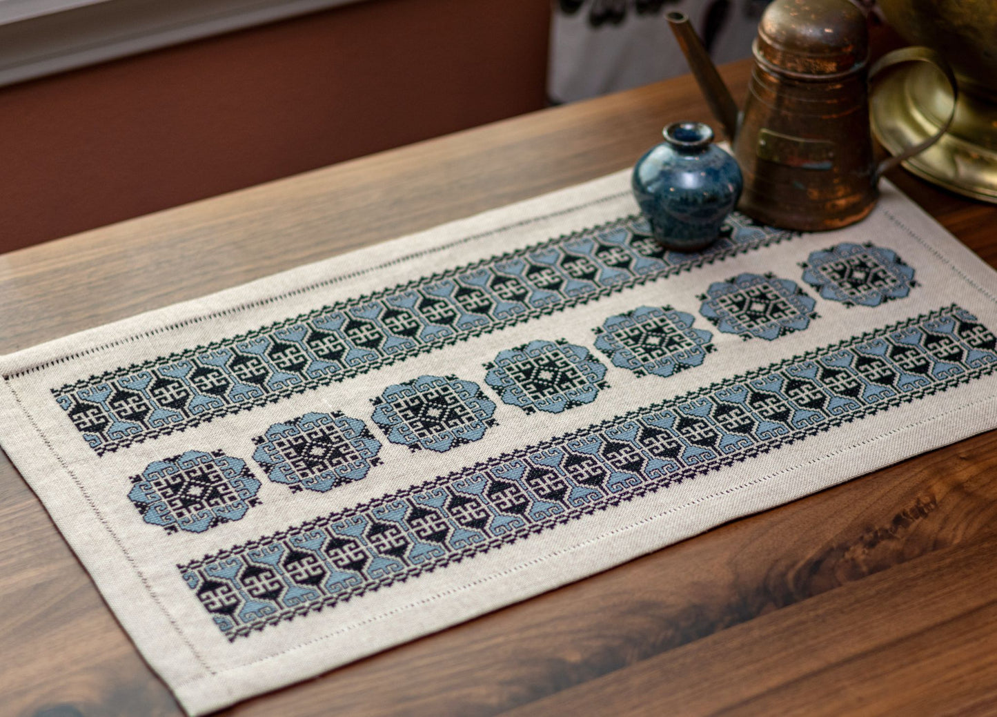 cross stitch folk embroidery with blue floral motif on flax linen with copper jug and vase