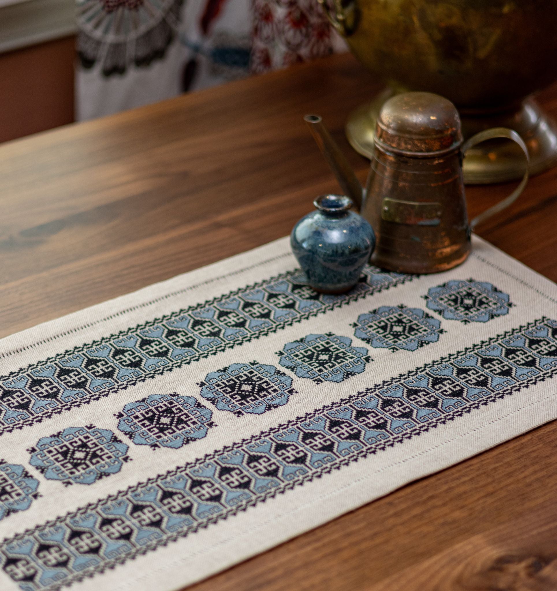 cross stitch folk embroidery with blue floral motif on flax linen with copper jug and vase