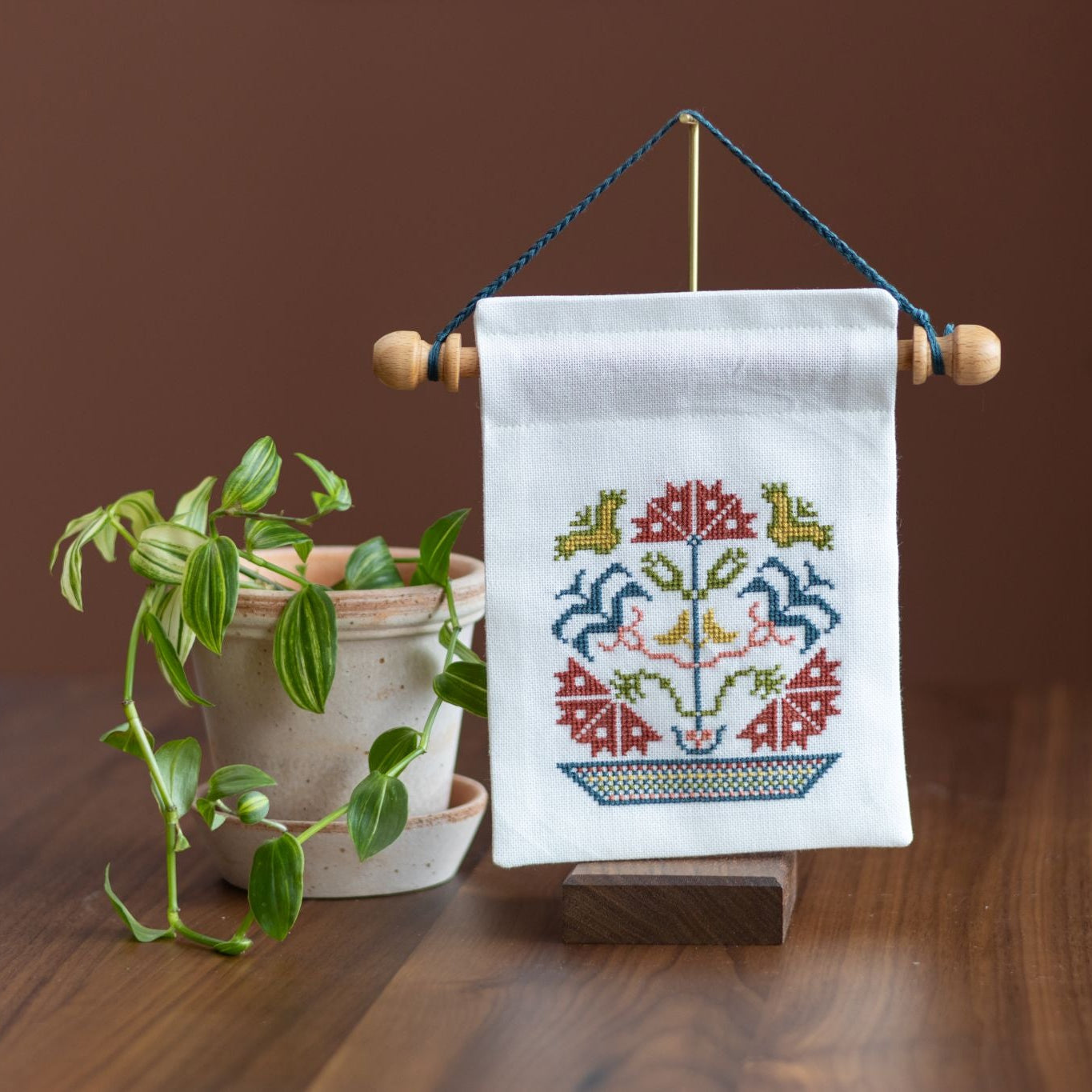 mini cross stitch folk embroidery wall hanging on stand with plant