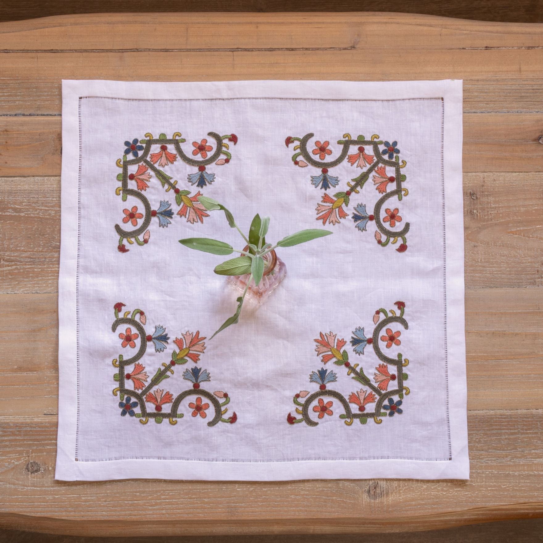 floral folk embroidery on white linen with pink vase on wood table