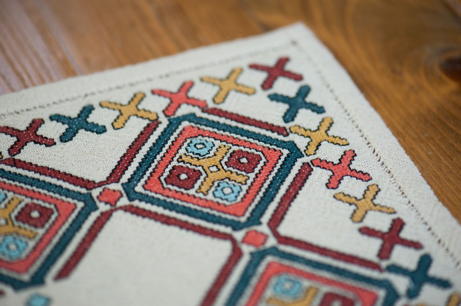 Close-up of a cross-stitched pattern on fabric with a wooden surface in the background