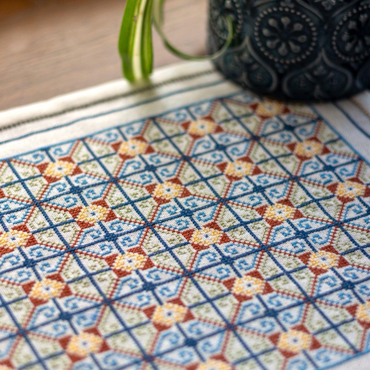 cross stitch folk embroidery repeating pattern closeup on table with plant