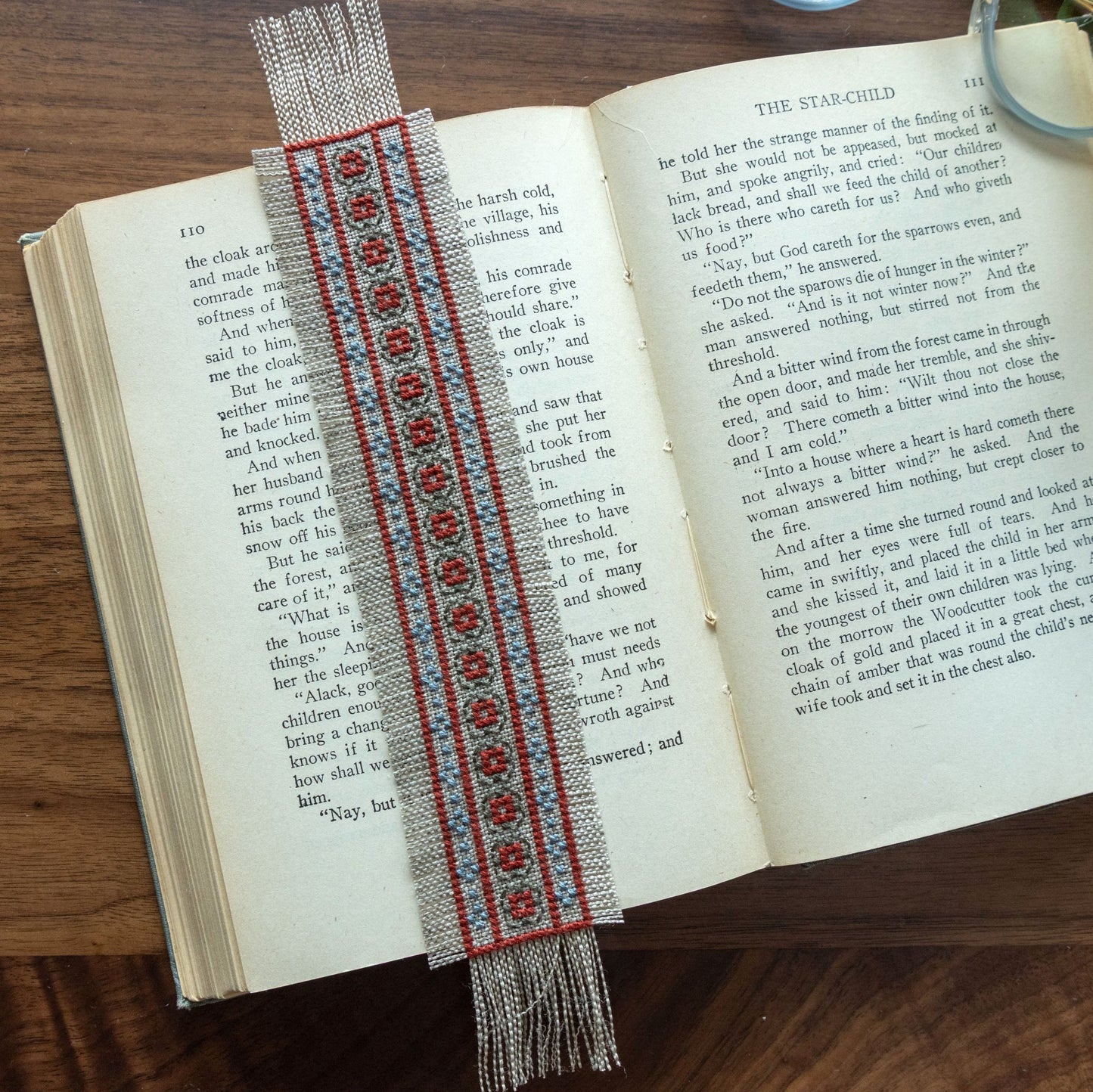 Decorative cross stitch bookmark with red and blue patterns on an open book