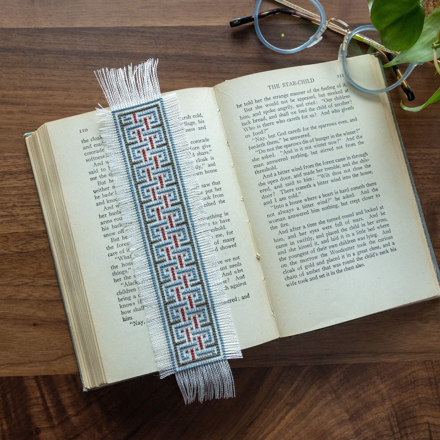 Open book with a decorative cross stitch bookmark on a wooden surface