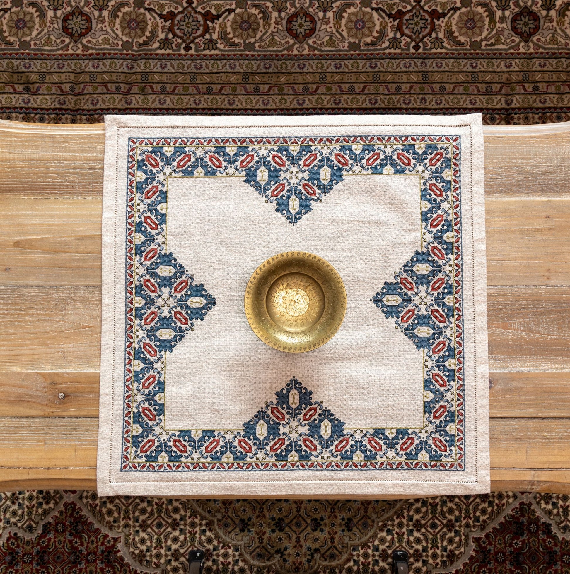 cross stitch folk embroidery textile with mulberry leaf pattern on table with ornate rug