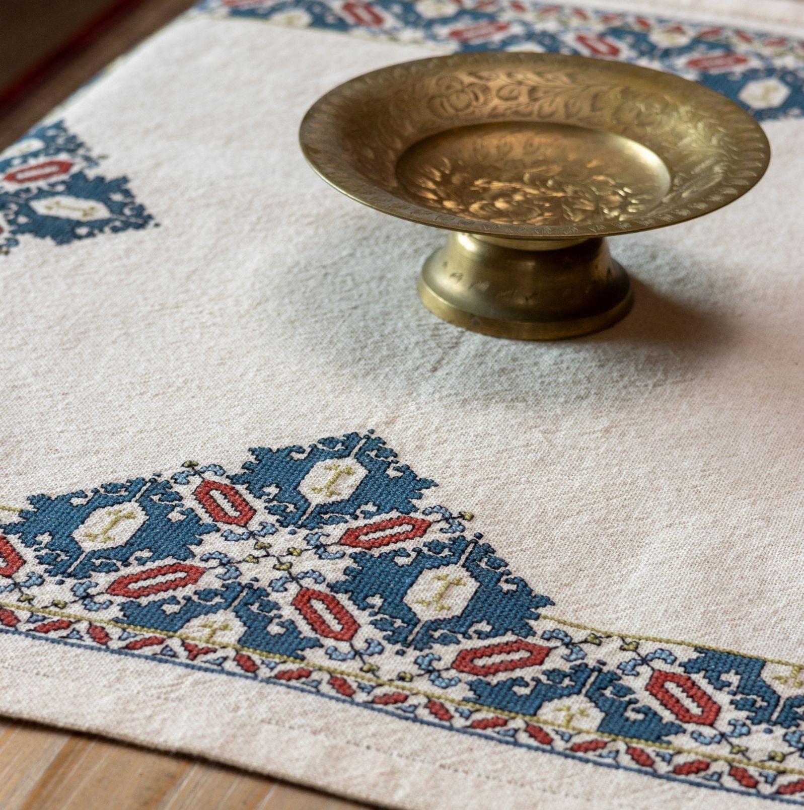 cross stitch folk embroidery textile with mulberry leaf pattern with brass dish on table