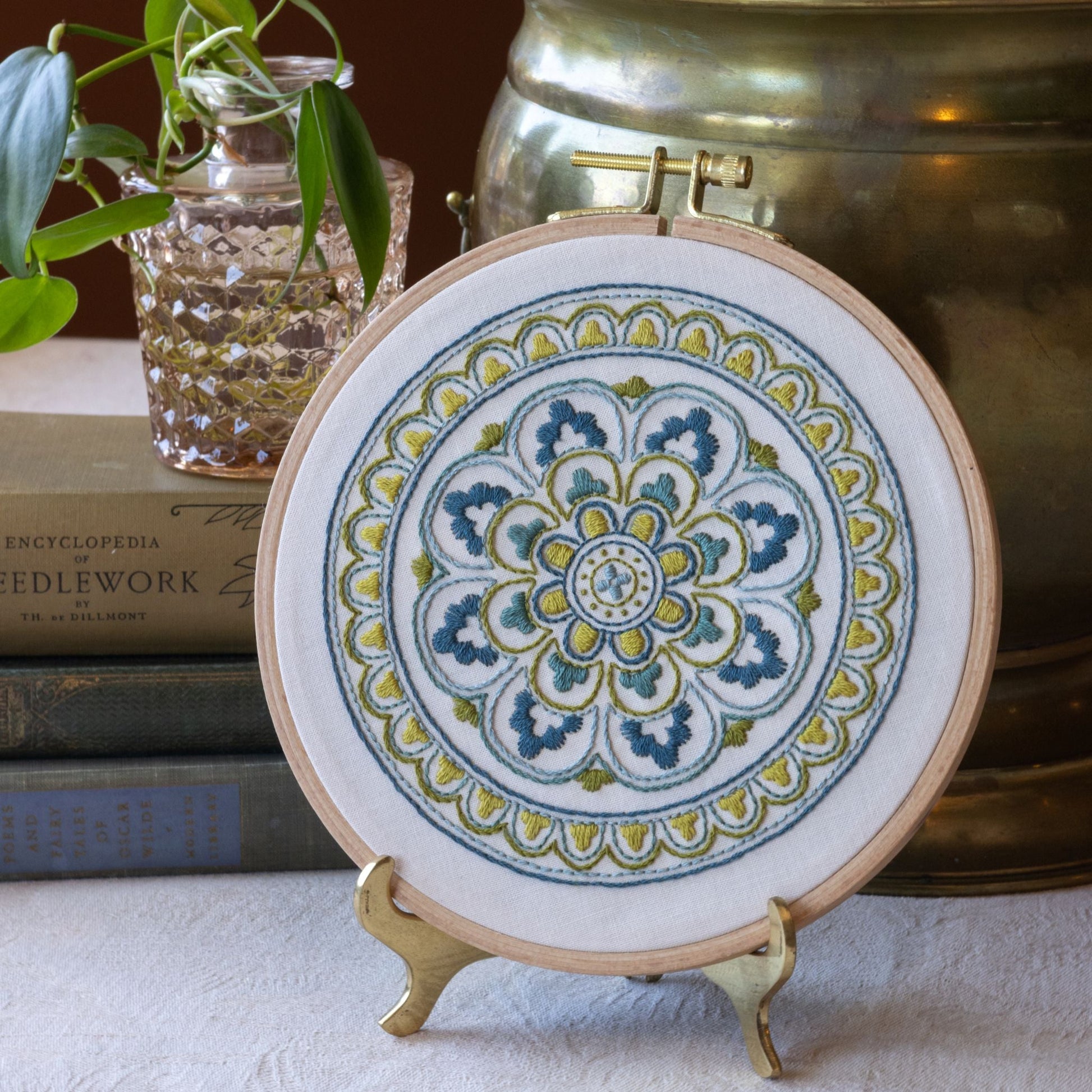 Decorative mandala embroidery, placed on a surface with books and plants in the background.