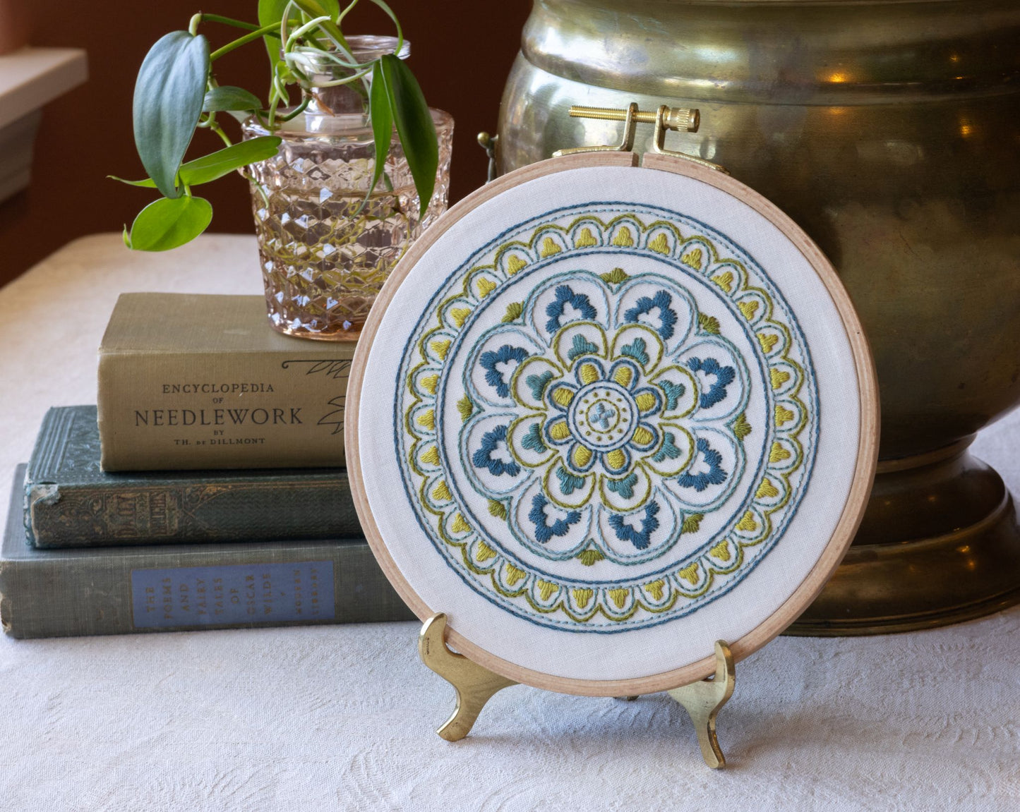 Decorative mandala embroidery  hoop with books and a plant in the background.