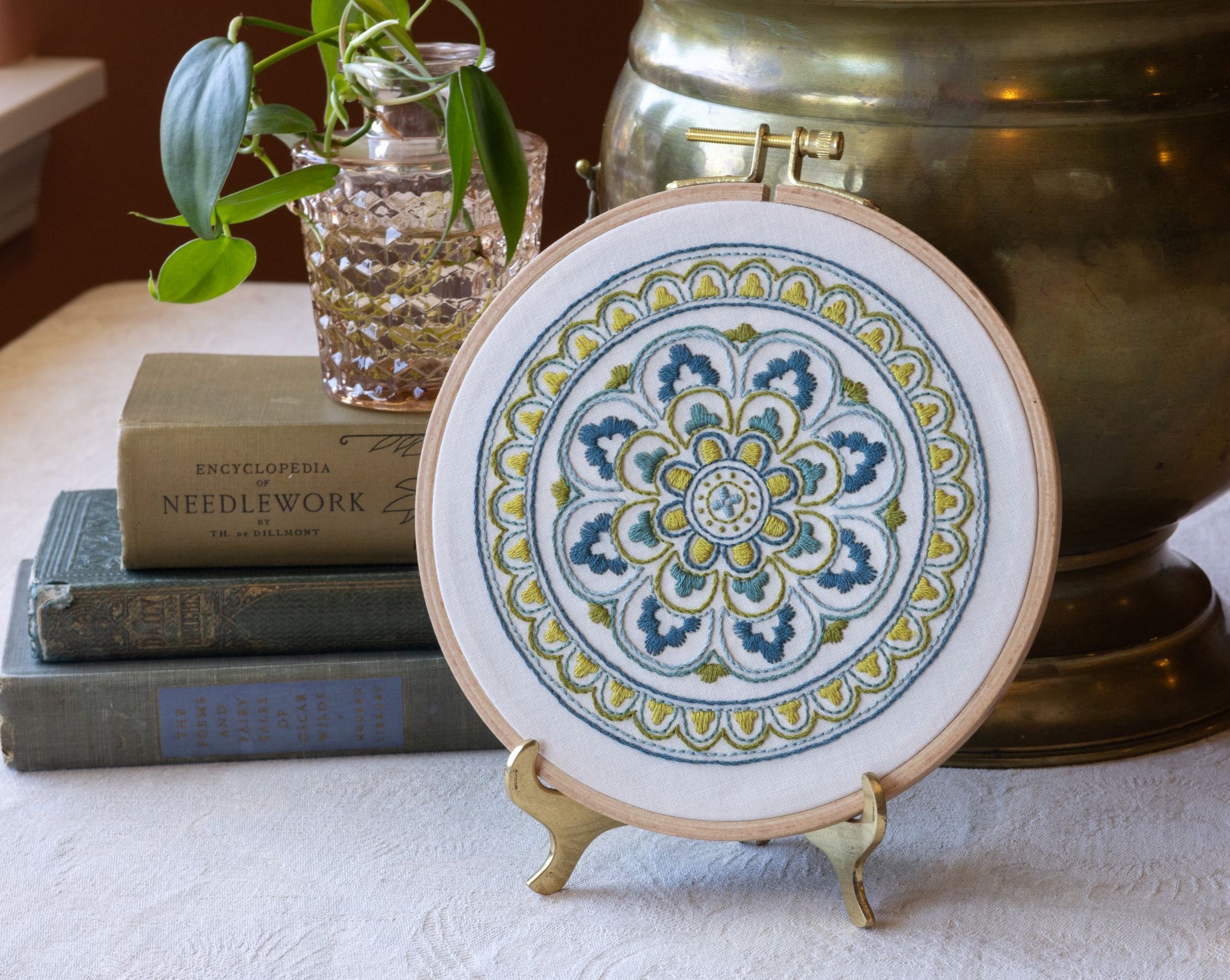 Decorative mandala embroidery  hoop with books and a plant in the background.