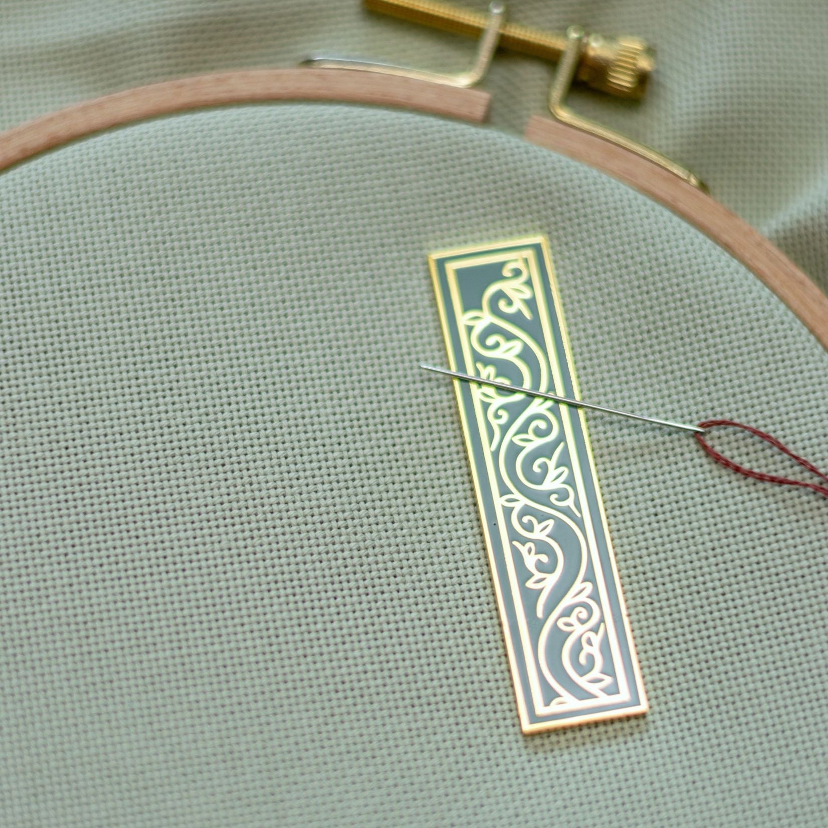 Embroidery hoop with a piece of fabric and a patterned enamel needleminder
