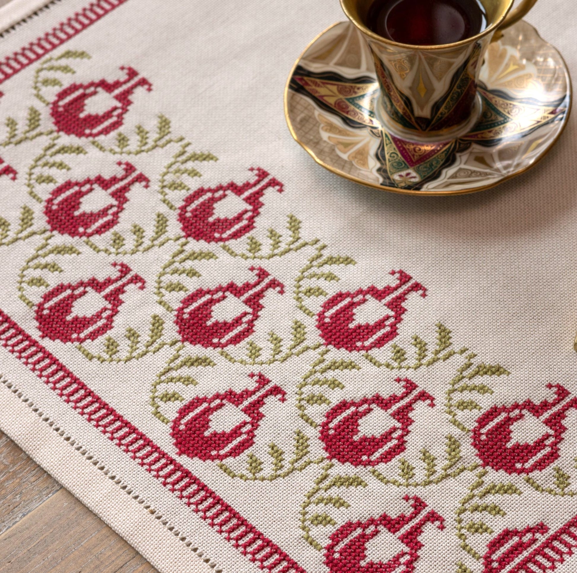Decorative tablecloth with pomegranate pattern and a cup of tea on a saucer.