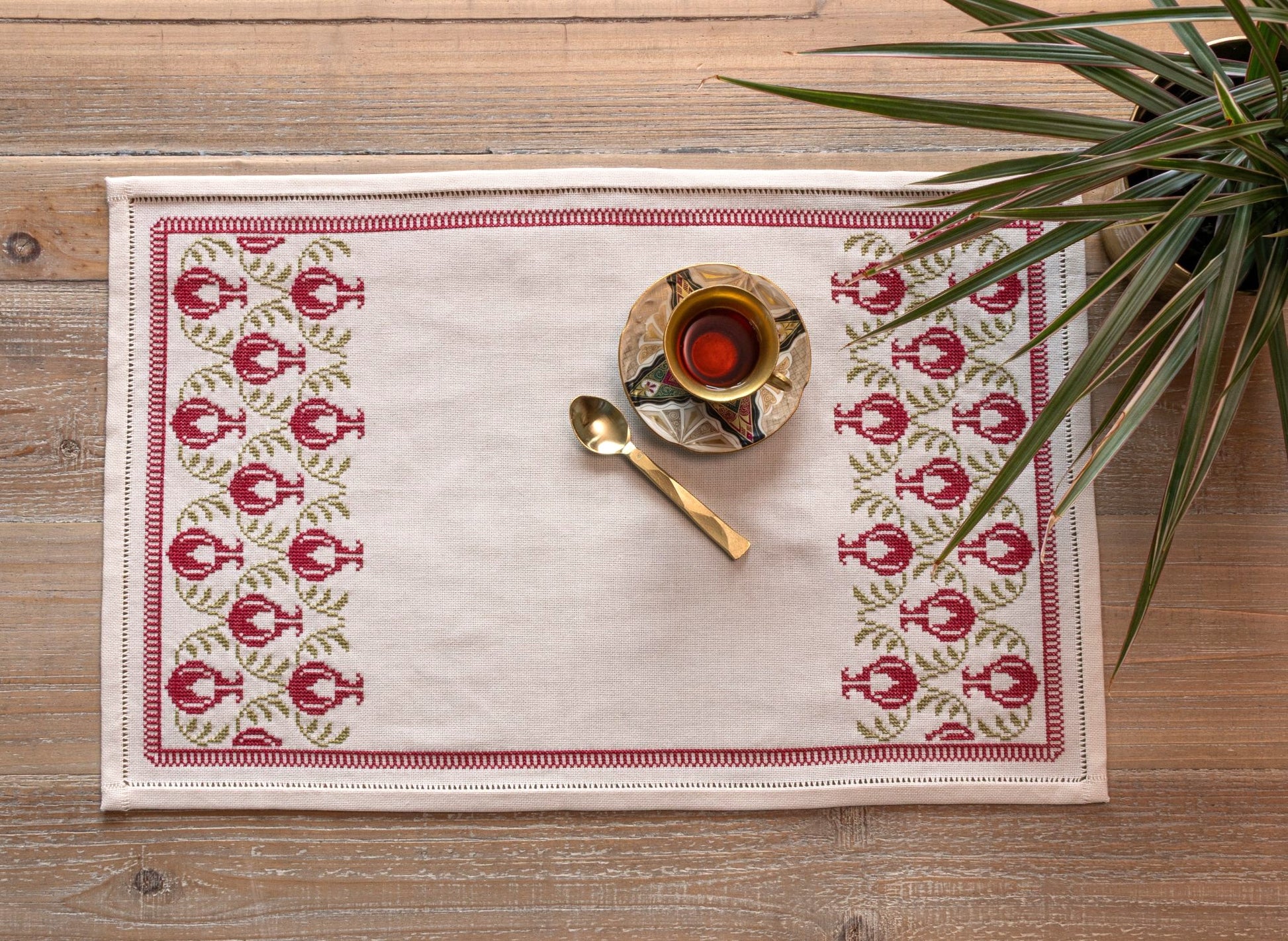 cross stitch table runner with pomegranate folk embroidery motif on wooden table with cup and spoon