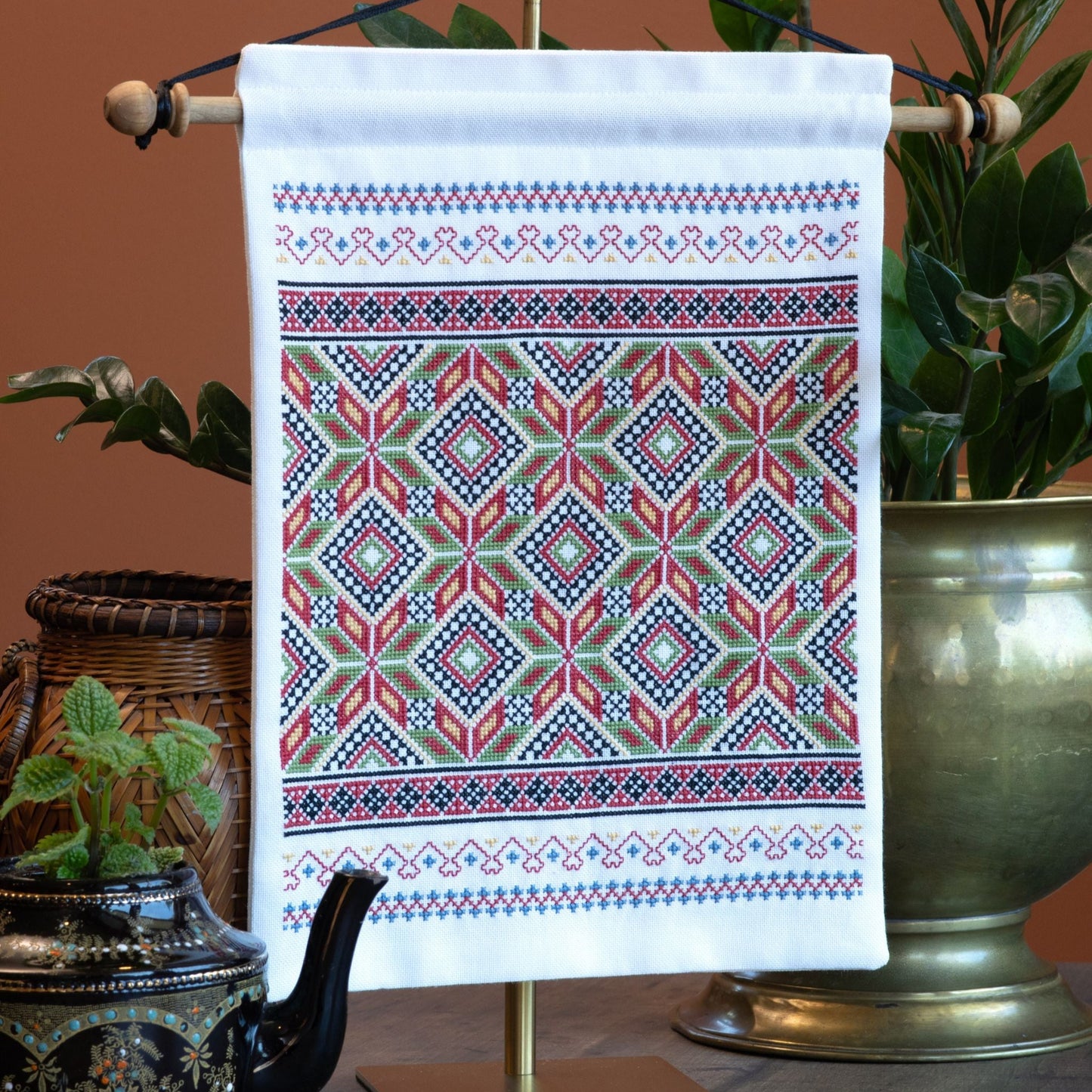 Decorative cross stitch wall hanging with geometric pattern on a stand against a brown background