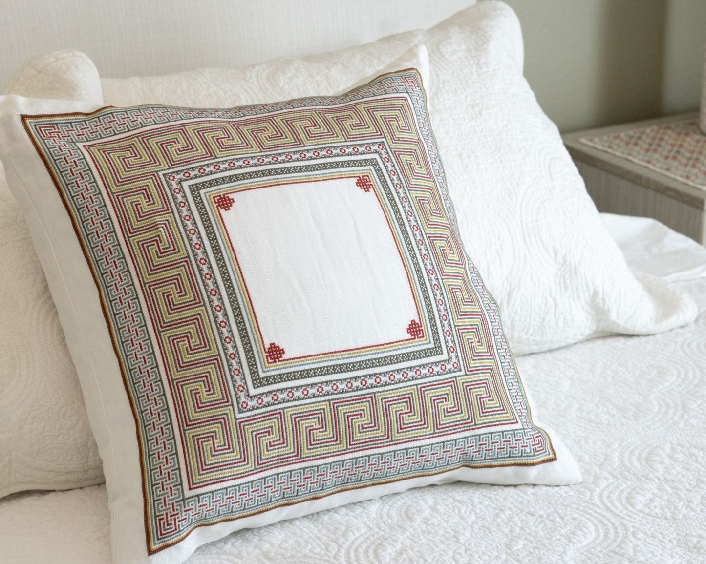 Somerset Meander cross stitch folk embroidery cushion cover in brown-grey, terra cotta and gold, on a bed