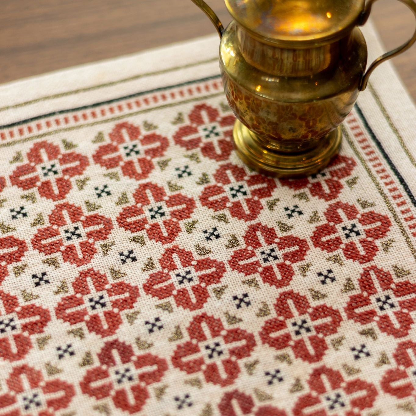 folk embroidery with repeating flower design in red, black and metallic thread closeup