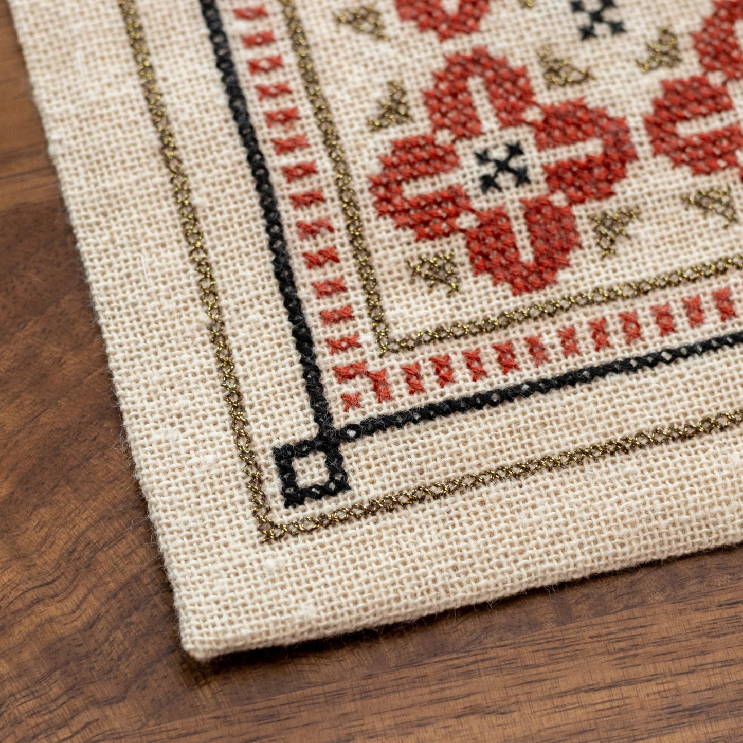 folk embroidery with repeating flower design in red, black and metallic thread closeup