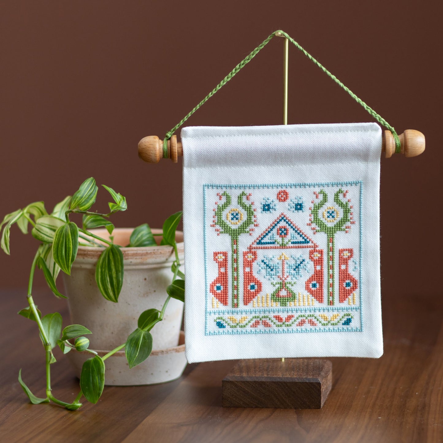 mini cross stitch folk embroidery wall hanging on stand with plant