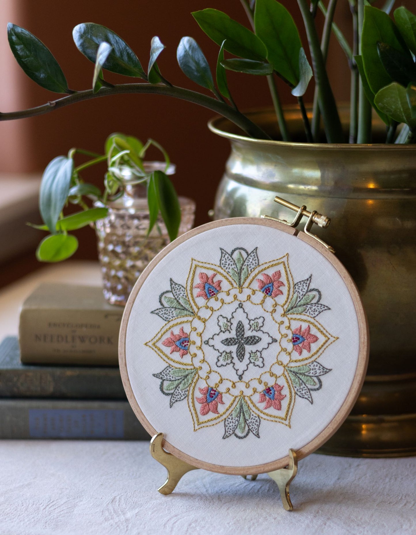 Embroidered mandala hoop art on a stand with plants and books in the background