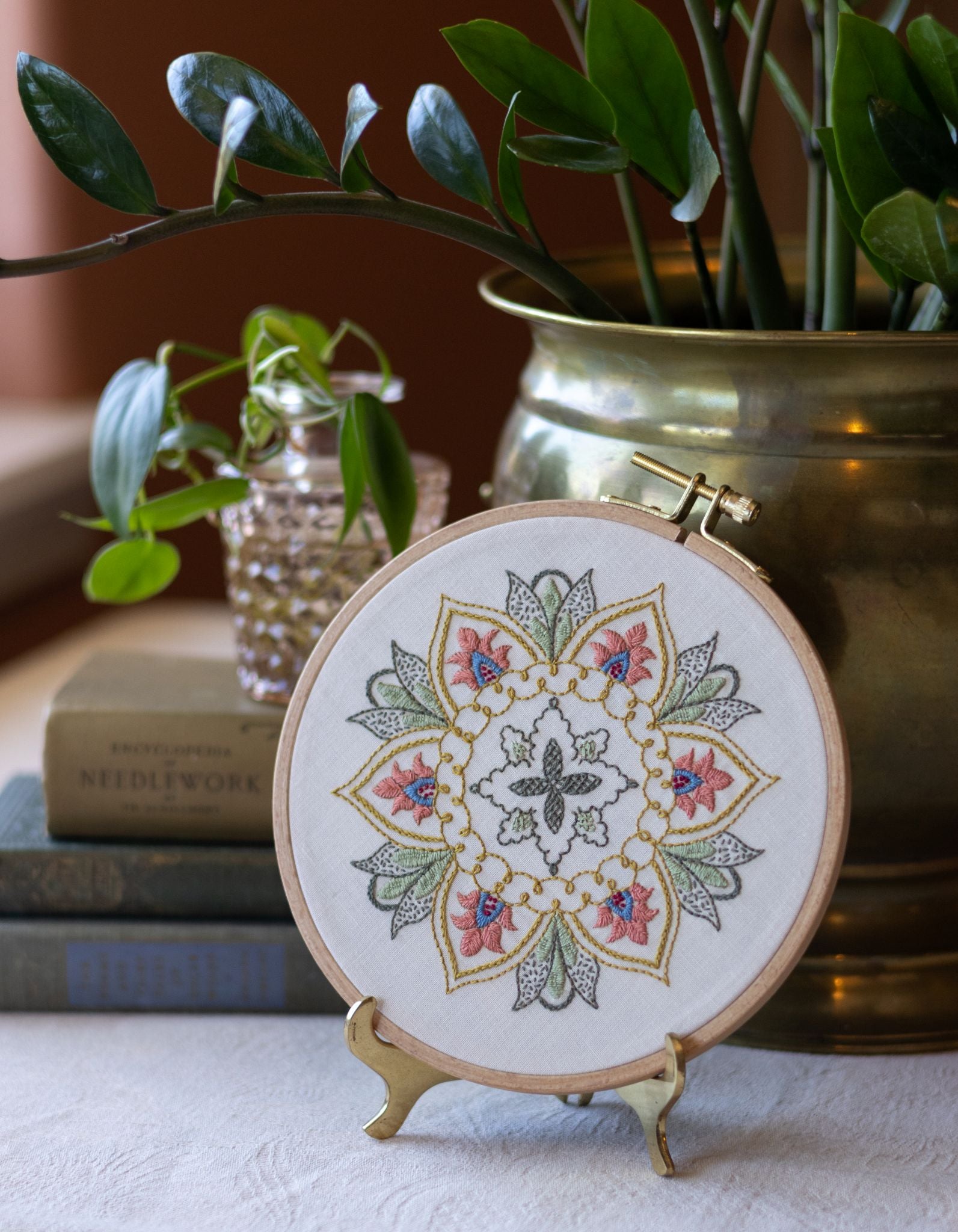 Embroidered mandala hoop art on a stand with plants and books in the background