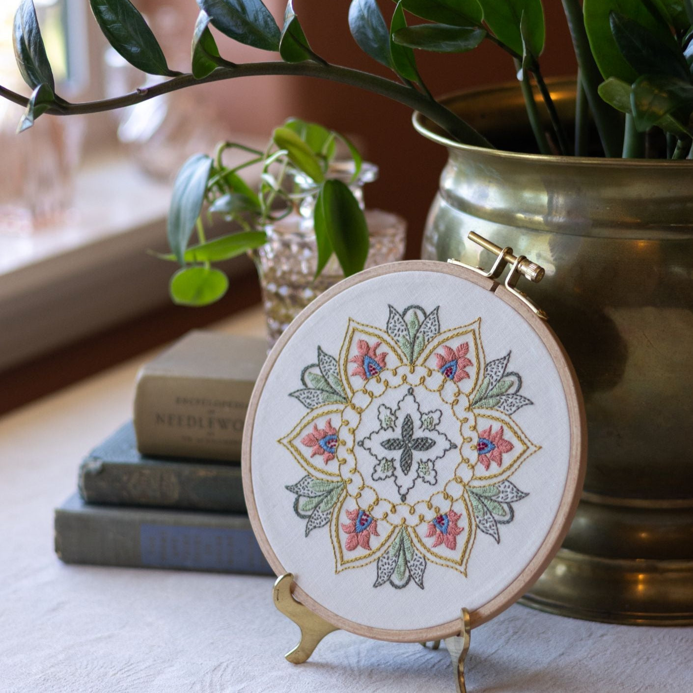 Embroidery hoop with mandala design on a stand next to a potted plant