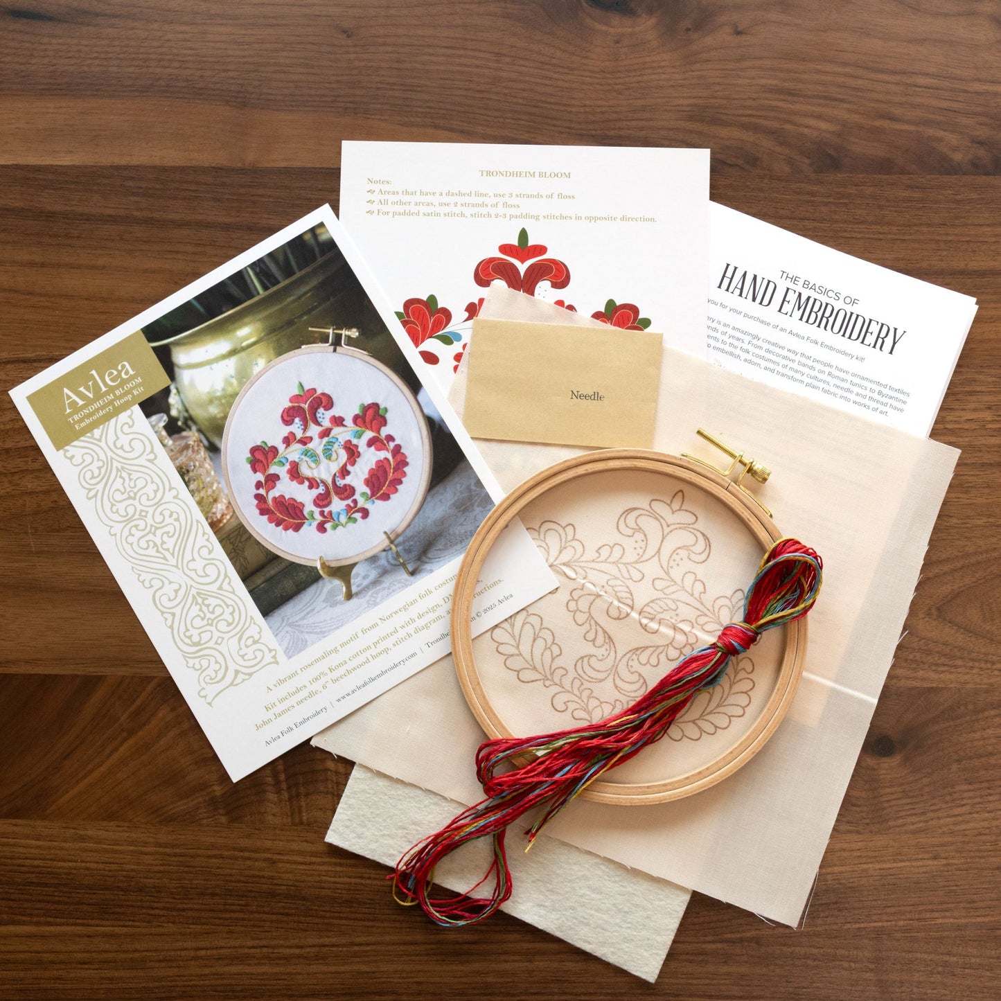 Embroidery hoop with red thread, patterned paper, and wooden box on a wooden surface