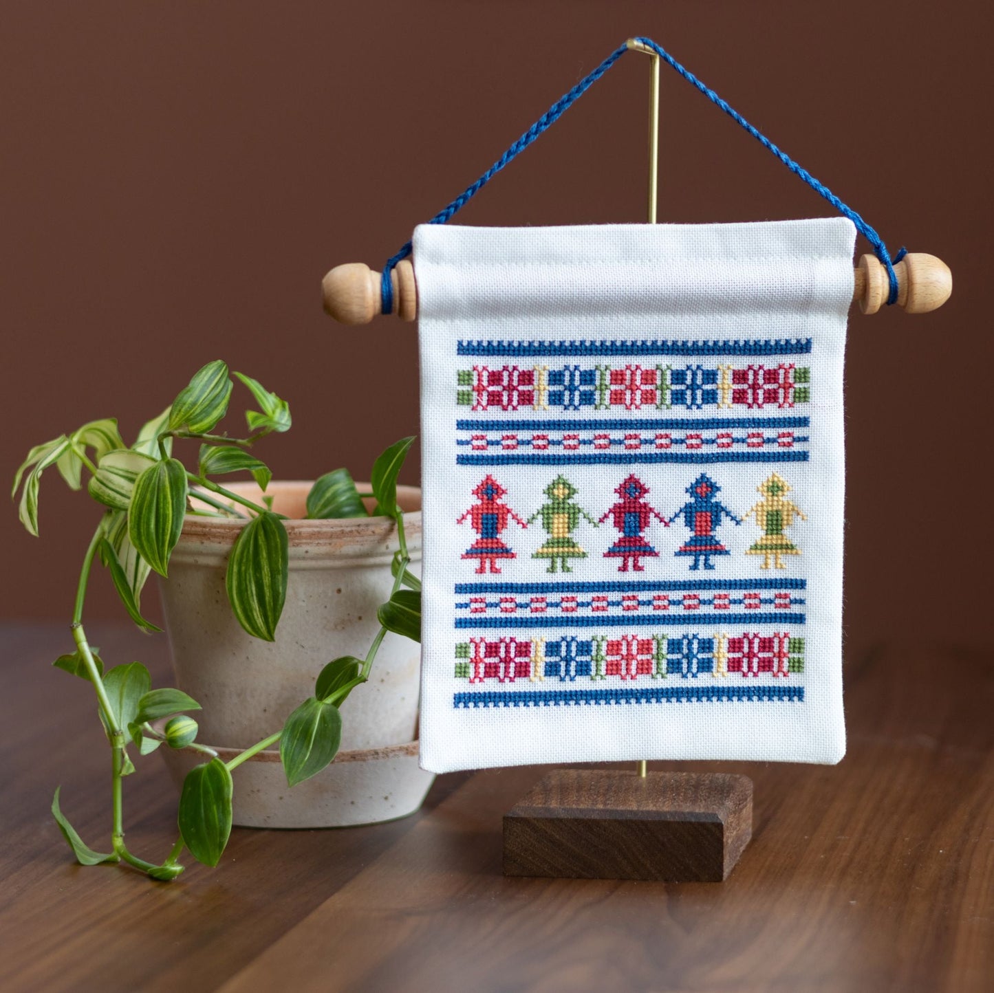 mini cross stitch folk embroidery wall hanging on stand with plant